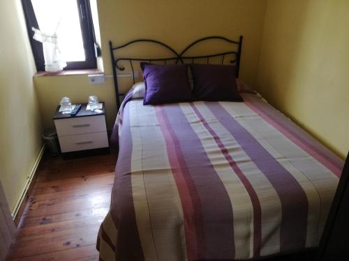 a bedroom with a bed with a striped comforter and a window at Pensión Rosa in Cabezón de la Sal