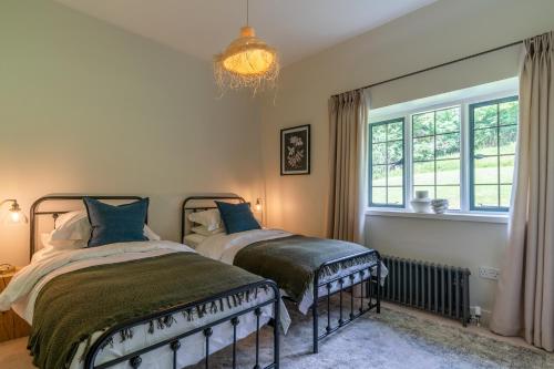 two beds in a bedroom with a window and a chandelier at Court Cottage in Stroud