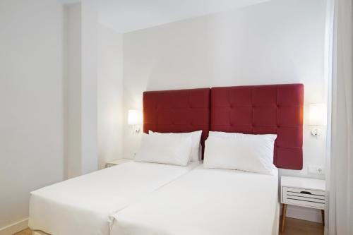 a bedroom with a large white bed with a red headboard at Apartamentos Metrópolis in Seville