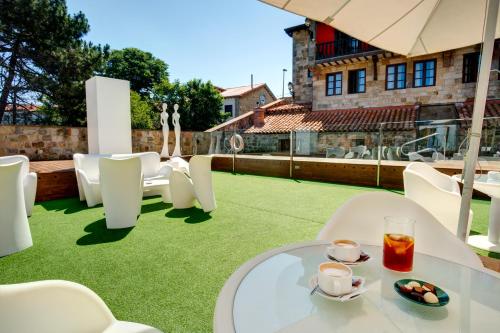 un patio con sillas blancas y una mesa con una bebida en Costa Esmeralda Suites, en Suances