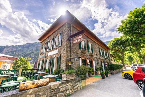 un edificio con mesas y coches estacionados frente a él en La Bonne Auberge, en Saint-Martin-Vésubie