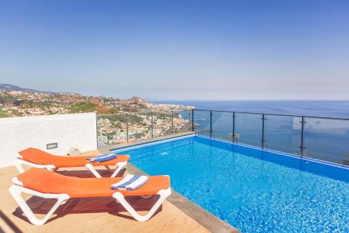 a swimming pool with two chairs and the ocean at Villa Amplitude in Câmara de Lobos