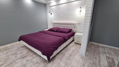 1 dormitorio con 1 cama con sábanas moradas y pared de ladrillo en Аpartaments on Metalurhiv 34, en Krivoy Rog