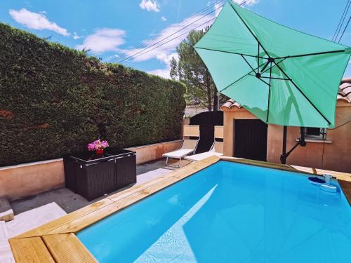 a swimming pool with a green umbrella next to a house at STUDIO PRIVATIF CLIMATISÉ , TERRASSE ET PiSCINE in Pernes-les-Fontaines