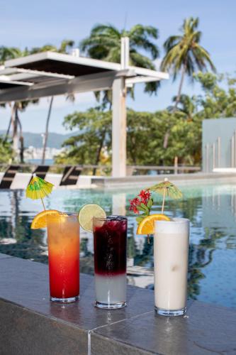 3 cocktails assis sur une table à côté d'une piscine dans l'établissement Ramada by Wyndham Acapulco Hotel & Suites, à Acapulco