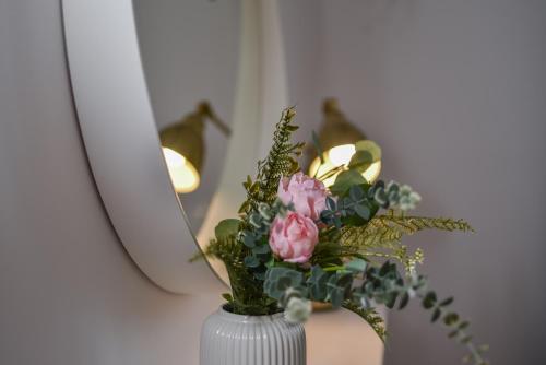 a white vase with pink flowers in front of a mirror at Lagom apartment Maribor w free parking & WiFi, tourist TAX included in Maribor