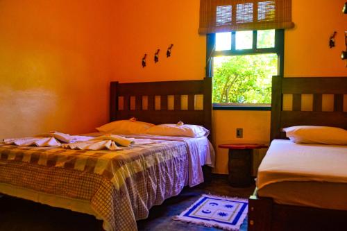 two beds in a room with orange walls and a window at Pousada Das Cores in Cumuruxatiba