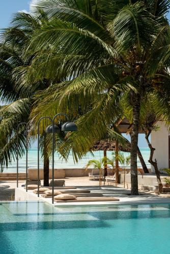 a swimming pool with palm trees next to a beach at Casa Beach Hotel "Casa Del Mar" in Jambiani
