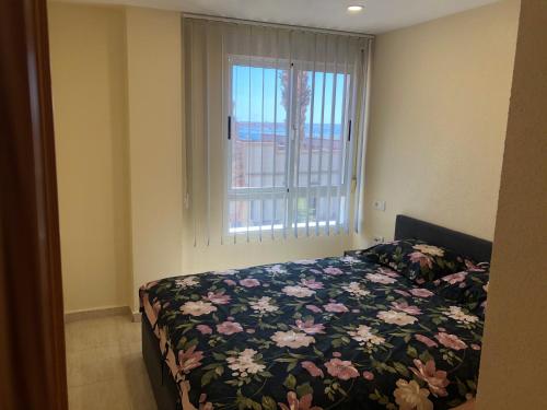 a bedroom with a bed with a floral comforter and a window at Apartament Claudia II in Puerto de Mazarrón