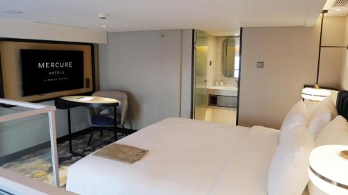 um quarto de hotel com uma cama branca e uma televisão em Mercure Surabaya Manyar em Surabaya
