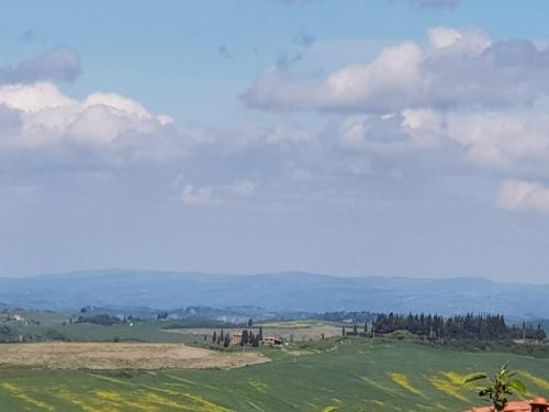 a green field with trees and clouds in the sky at Dimora in San Quirico d'Orcia in San Quirico dʼOrcia
