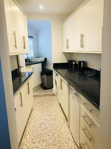 una cocina con armarios blancos y encimeras negras en The Borough apartment, en Kent