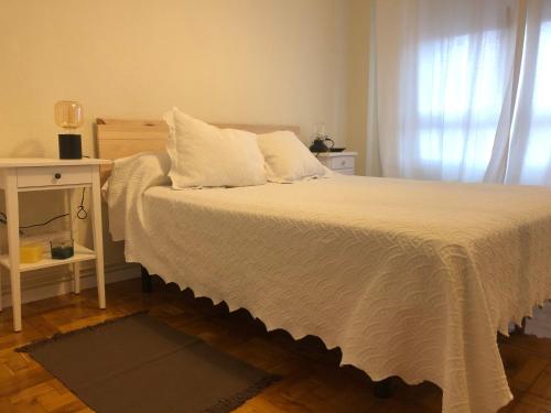 a bedroom with a white bed with a table and a window at Casa en la playa in Gijón