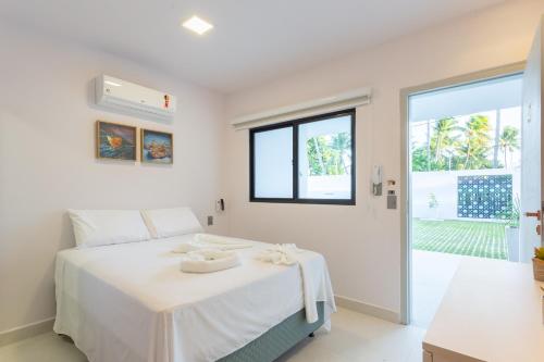 a white bedroom with a bed and a window at Quinta do Mar Flats Porto de Galinhas in Porto De Galinhas