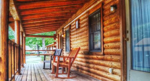 a porch of a log cabin with two chairs and a table at Crown Lake Resort in Horseshoe Bend