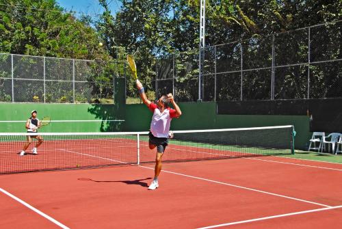 een man die een tennisbal serveert op een tennisbaan bij Guacamaya Lodge in Paraíso