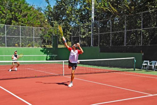a man serving a tennis ball on a tennis court at Guacamaya Lodge in Paraíso