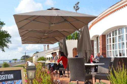 a group of people sitting at tables under an umbrella at Hotel et Spa Les Cleunes Oléron in Saint-Trojan-les-Bains