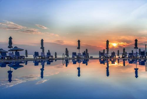 a sunset over a pool with chairs and umbrellas at Acrotel Lilyann Boutique Hotel in Elia