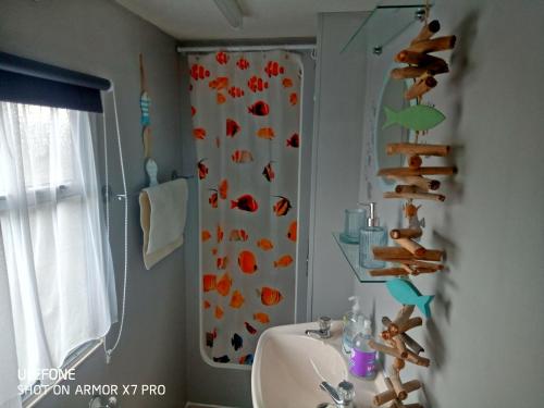 baño con lavabo y cortina de ducha con pescado. en Gina's Static caravan,118 Sandsgate en Hemsby