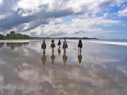 a group of people riding horses on the beach at Guacamaya Lodge in Paraíso