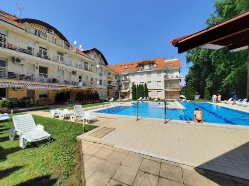 a swimming pool with chairs and a person standing next to a building at Hajdúszoboszló Toscana Panoráma in Hajdúszoboszló