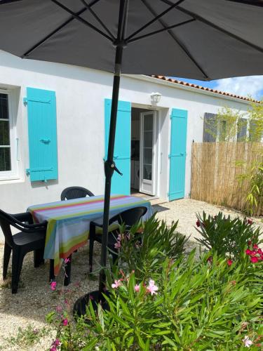 une table et des chaises sous un parasol devant une maison dans l'établissement Le sable chaud, à Saint-Pierre-dʼOléron