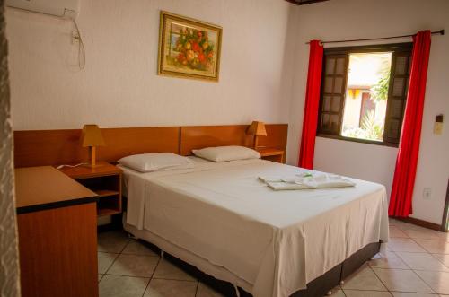a bedroom with a bed and a window with red curtains at Pousada Lapônia in Penedo