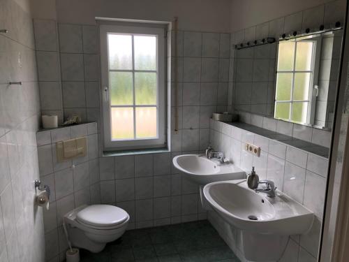 een badkamer met 2 wastafels, een toilet en een raam bij Kapitänshaus Scharmberg, Ferienwohnung Seeadler in Born