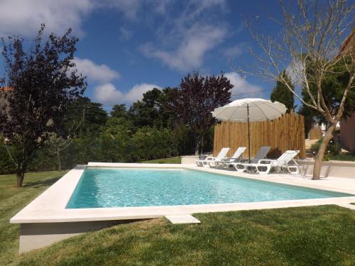 a swimming pool with chairs and an umbrella at Casal do Pinheiro in Óbidos