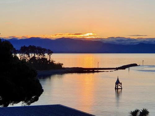 a person standing on a boat in the water at sunset at Kimberley Three - Nelson Waterfront Penthouse in Nelson