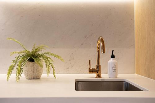 een wastafel met een fles zeep naast een plant bij Luxuria Apartments - Collins House in Melbourne