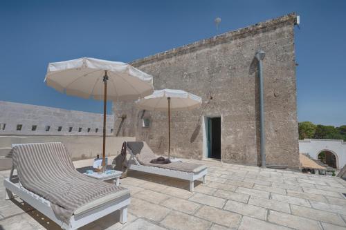 two chairs and umbrellas on a patio in front of a building at Masseria Palombara Relais & SPA - Adults only in Manduria