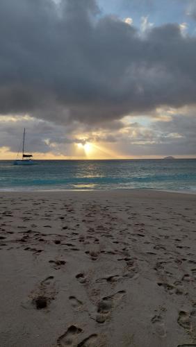 a beach with footprints in the sand with a sail boat in the water at Maison Ed-Elle in La Digue