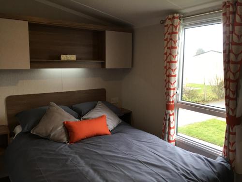 a bed with an orange pillow sitting next to a window at 3 Bed Luxury Mobile Home Hoburne Park Christchurch in Christchurch