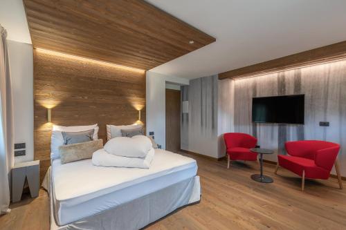 a bedroom with a bed and a television and red chairs at Cima Dodici B&B - Apartments in Sesto
