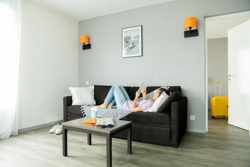 a woman laying on a couch in a living room at Aparthotel Adagio Access Orléans in Orléans