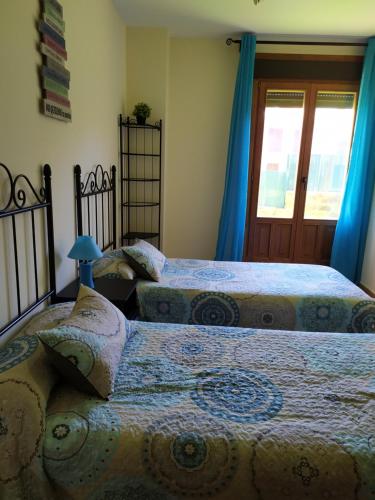 a bedroom with two beds with blue curtains and a window at Playa, Golf y Montaña. Dos países, un lugar único. in Huelva
