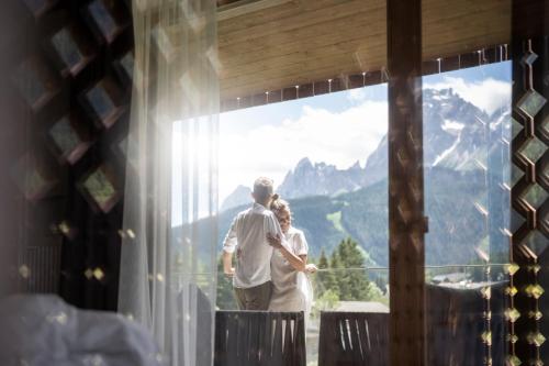 a man and woman looking out of a window at mountains at Aparthotel Gamz in Sesto
