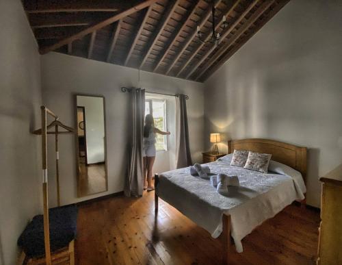 a woman standing in a bedroom looking out the window at Casa na Ribeira in Ribeira Grande