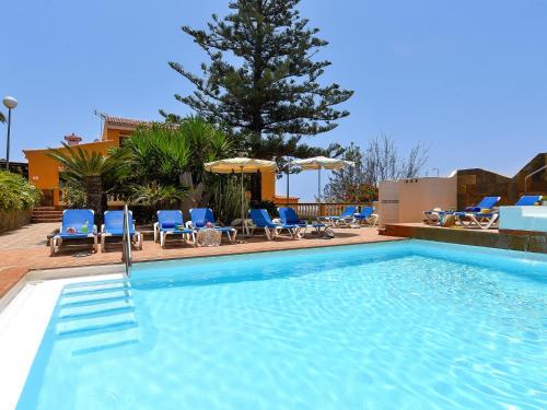 a large swimming pool with blue chairs and a tree at Rural Village Salobre by VillaGranCanaria in Maspalomas