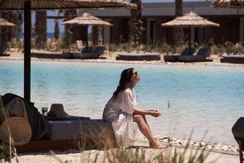a woman sitting on a bed next to a pool at Casa Cook North Coast - Adults Only in El Alamein