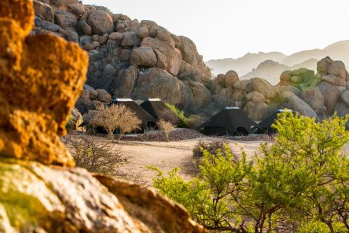 a group of buildings in a field next to some rocks at Ai Aiba - The Rock Painting Lodge in Omaruru