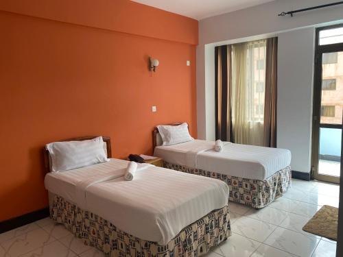 two beds in a room with an orange wall at Panama Inn Moshi in Moshi