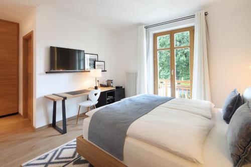 a bedroom with a bed and a desk with a television at Das Tegernsee in Tegernsee