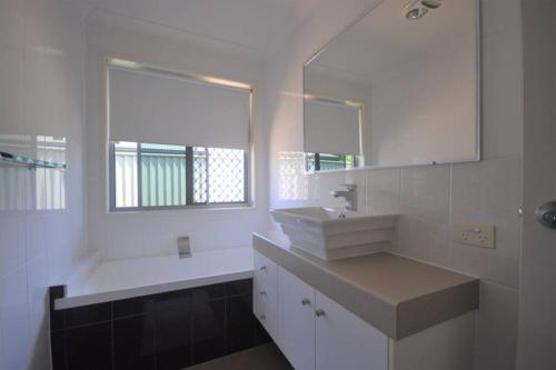 a white bathroom with a sink and a mirror at Home away from home - Modern luxury in central Bundaberg in Bundaberg