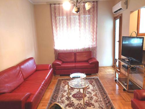 uma sala de estar com sofás de couro vermelho e uma televisão em Friendly City Centre em Podgorica