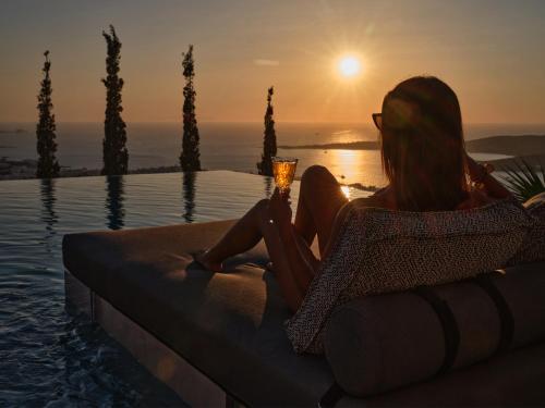 a woman sitting in a chair next to a pool watching the sunset at Infinity sea view hillside villa with private pool in Parikia