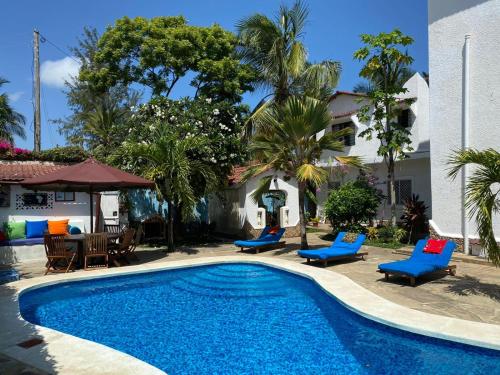 a swimming pool with blue chairs and a house at Luciano & Grace Apartments in Watamu