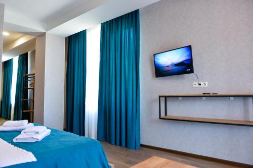 a bedroom with a television on a wall with blue curtains at Tskaltubo Epic Hotel & Spa in Tskaltubo